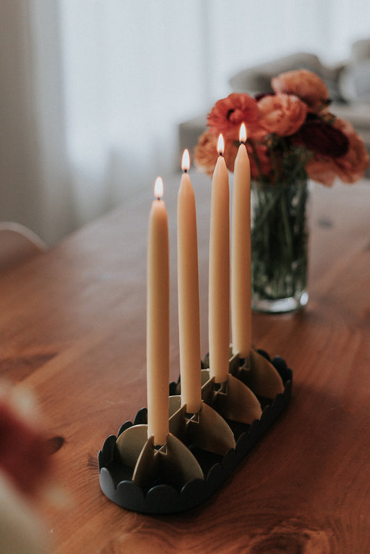 Beeswax Taper Candles lit in 4 candle holders on a dining room table.